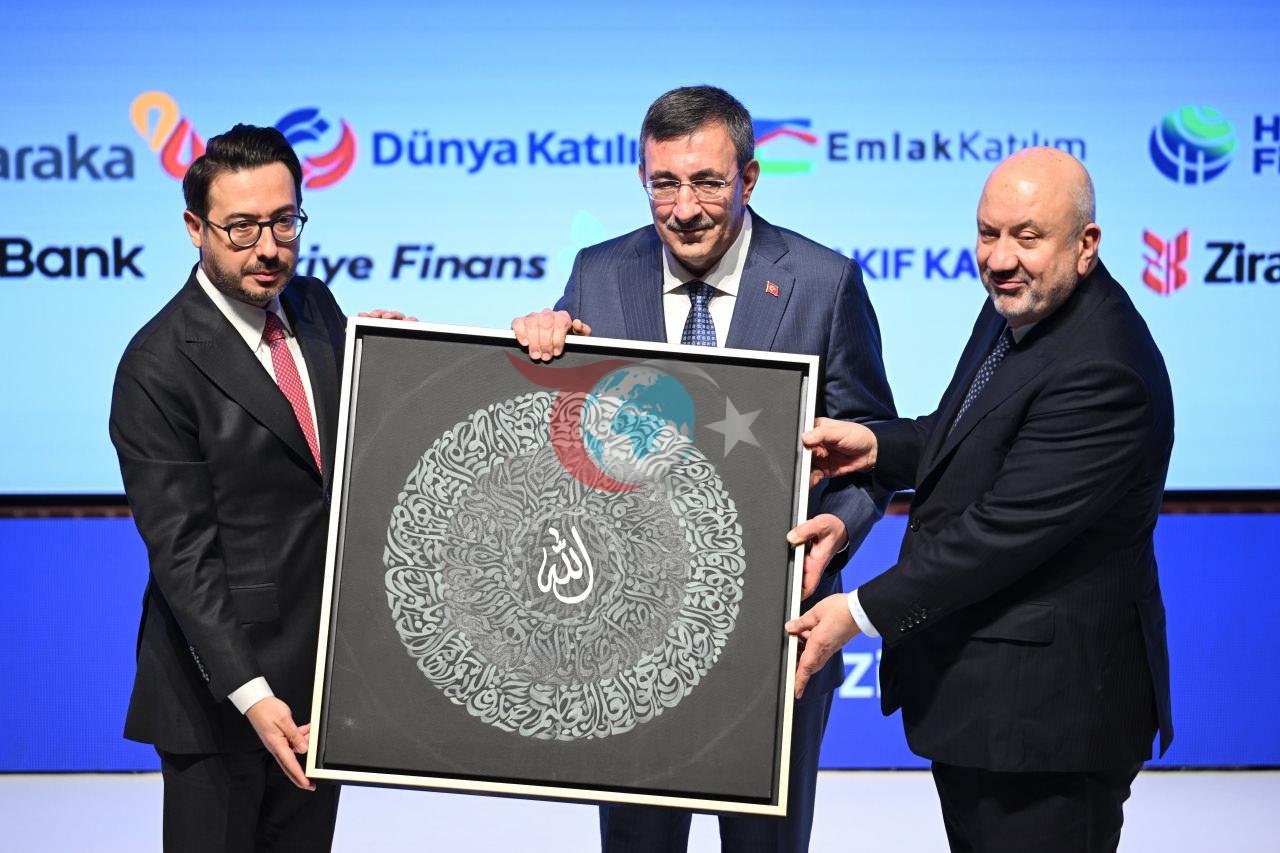  Anadolu Ajansı (AA) Yönetim Kurulu Başkanı ve Genel Müdürü Serdar Karagöz (solda), Türkiye Katılım Bankaları Birliği Başkanı Mehmet Ali Akben (sağda), zirveye katılan Cumhurbaşkanı Yardımcısı Cevdet Yılmaz'a (ortada) hediye takdim etti.